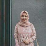 Portrait of a young woman wearing a hijab, smiling in an outdoor setting with a shoulder bag.
